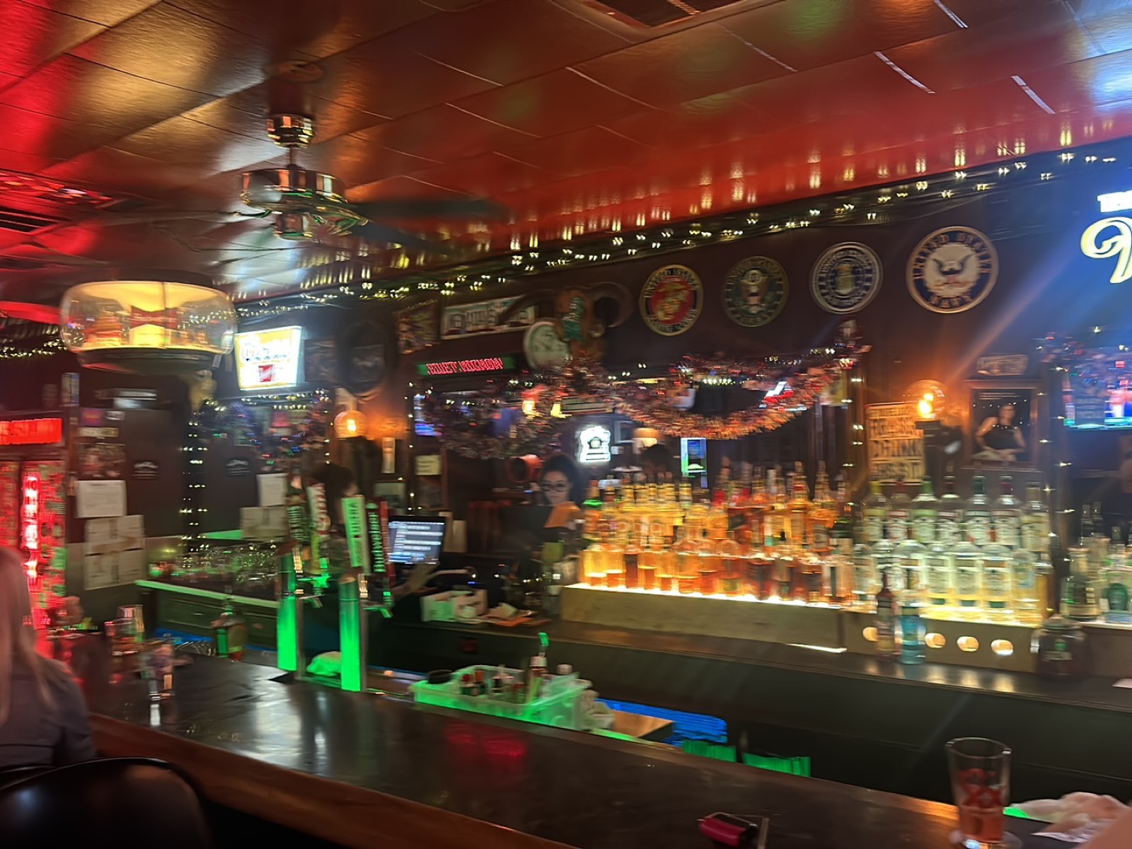 The saloon bar at night, lit by warm neon and lined with bottles.