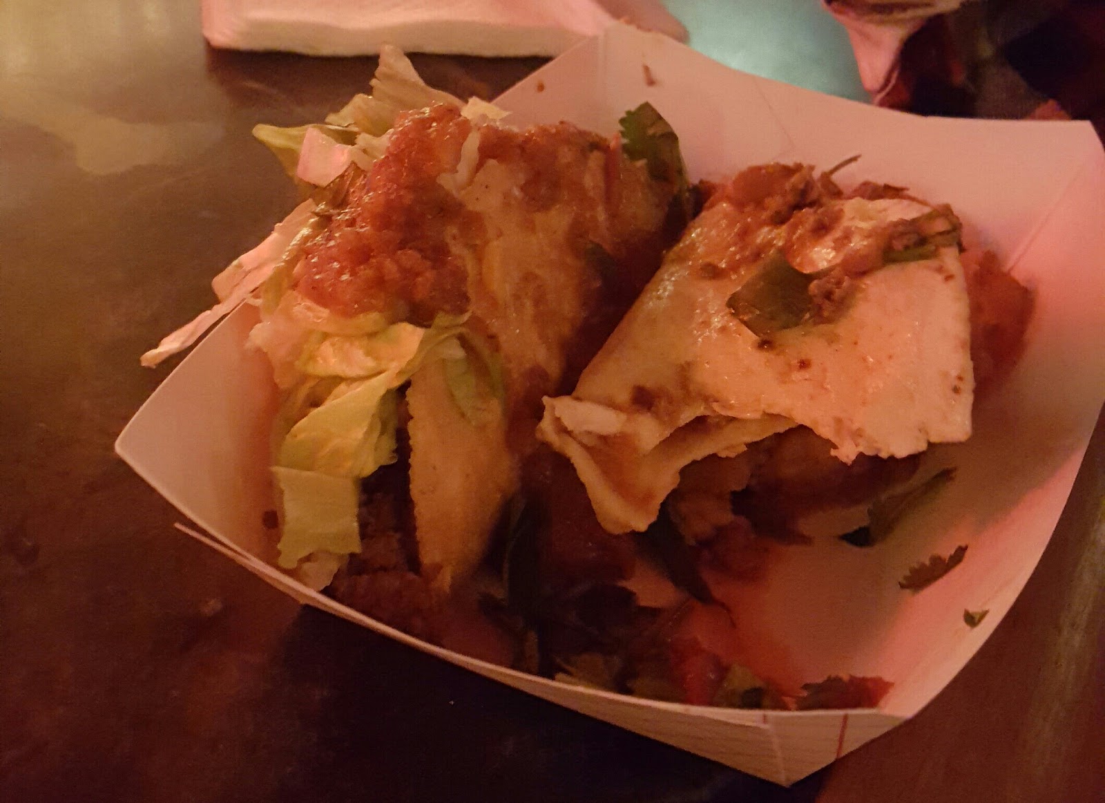 Two crispy tacos loaded with salsa in a paper tray.